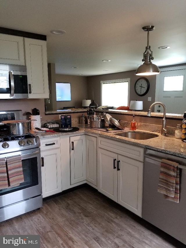 kitchen with sink, dark wood-type flooring, stainless steel appliances, pendant lighting, and white cabinets