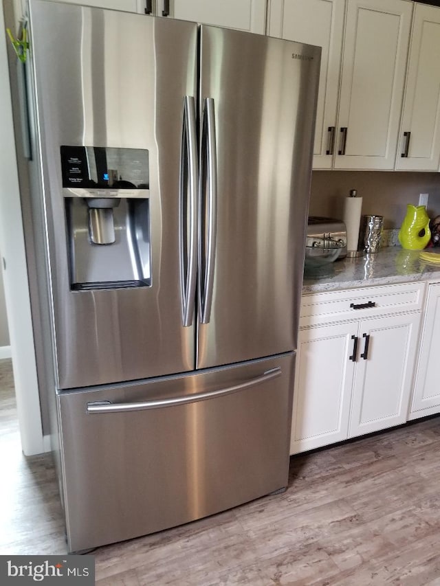 kitchen with light hardwood / wood-style floors, light stone countertops, stainless steel refrigerator with ice dispenser, and white cabinetry