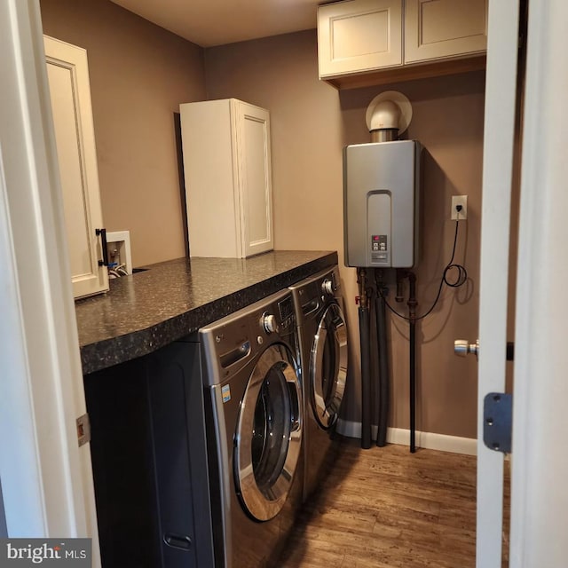 clothes washing area with hardwood / wood-style floors, tankless water heater, washing machine and dryer, and cabinets