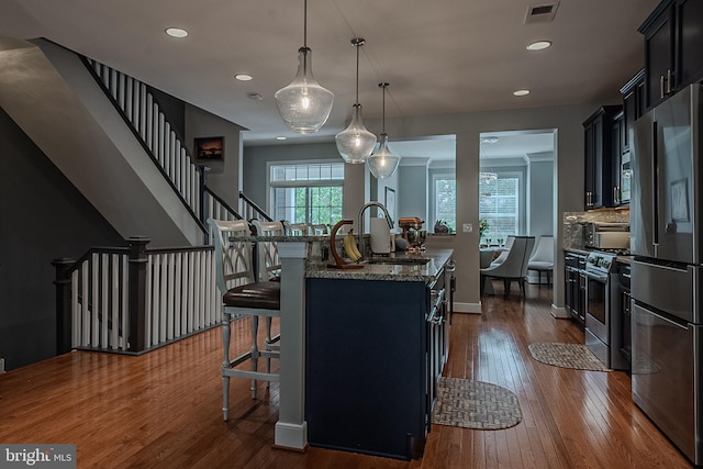 kitchen with a kitchen bar, appliances with stainless steel finishes, sink, a center island with sink, and hanging light fixtures