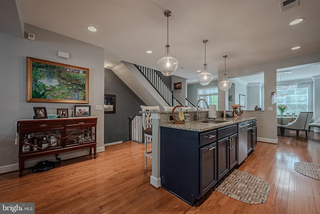 kitchen with sink, light stone counters, light hardwood / wood-style floors, decorative light fixtures, and a kitchen island with sink