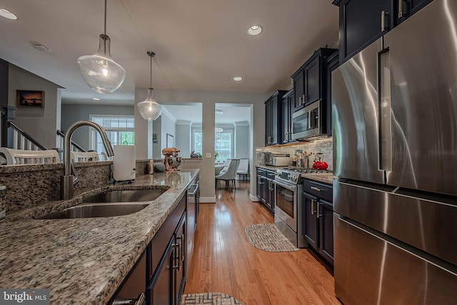 kitchen with light stone countertops, light wood-type flooring, stainless steel appliances, sink, and hanging light fixtures