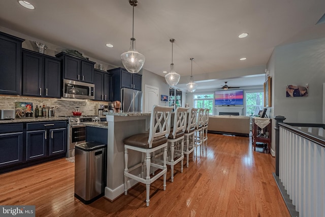 kitchen featuring tasteful backsplash, pendant lighting, a breakfast bar area, a center island with sink, and appliances with stainless steel finishes