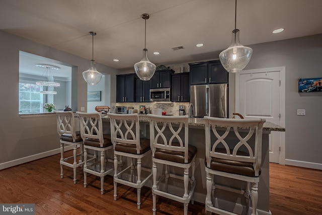 kitchen with a breakfast bar area, pendant lighting, an island with sink, and stainless steel appliances