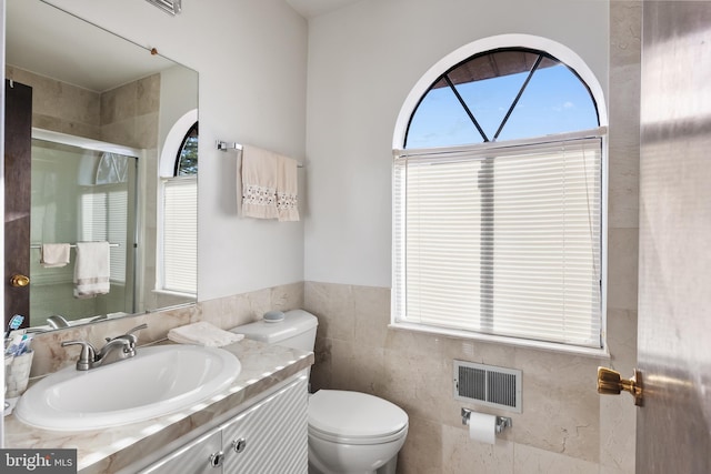 bathroom with walk in shower, vanity, toilet, and tile walls