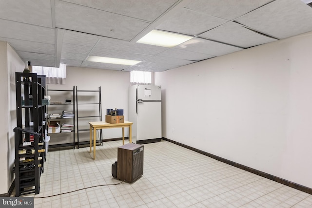 basement with white fridge and a drop ceiling