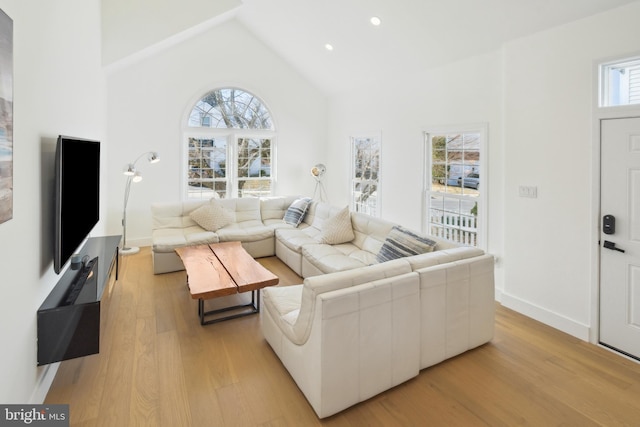 living room with plenty of natural light, light wood-style flooring, high vaulted ceiling, and baseboards