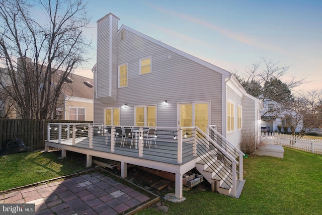 back of property at dusk featuring a deck, a chimney, a yard, and fence