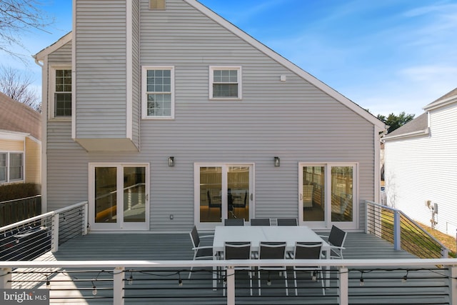 rear view of house with outdoor dining space, a chimney, and a wooden deck