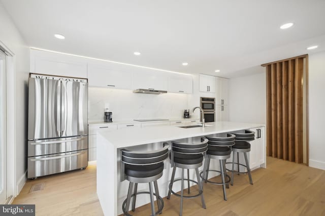 kitchen featuring light wood finished floors, light countertops, stainless steel appliances, white cabinetry, and a sink