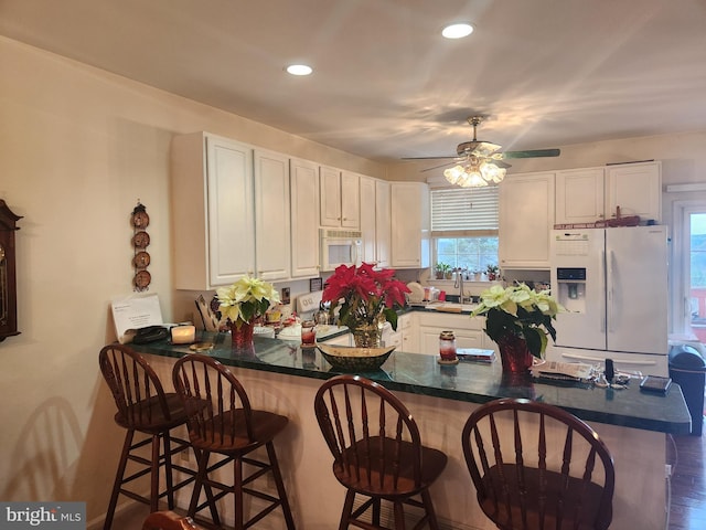 kitchen featuring kitchen peninsula, a breakfast bar, white appliances, and sink