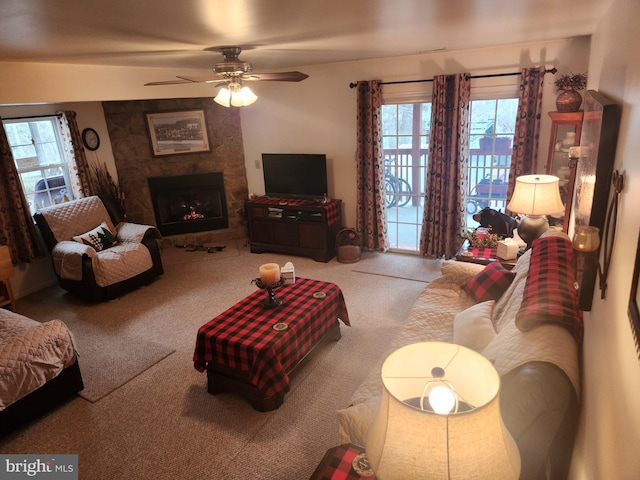 carpeted living room with a stone fireplace and ceiling fan