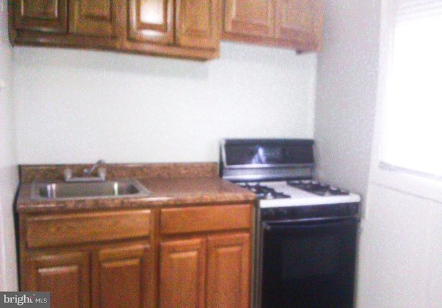 kitchen featuring white range with gas stovetop, sink, and fridge