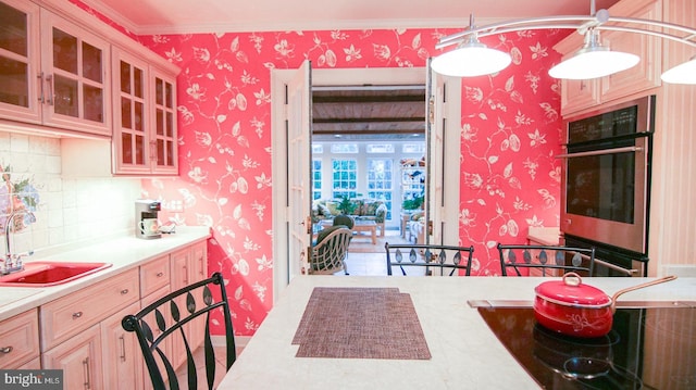 kitchen featuring decorative backsplash, ornamental molding, sink, light brown cabinets, and hanging light fixtures