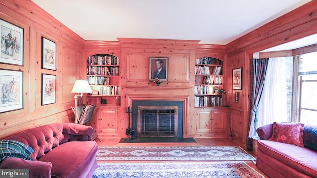 living room featuring built in shelves, wooden walls, and hardwood / wood-style flooring