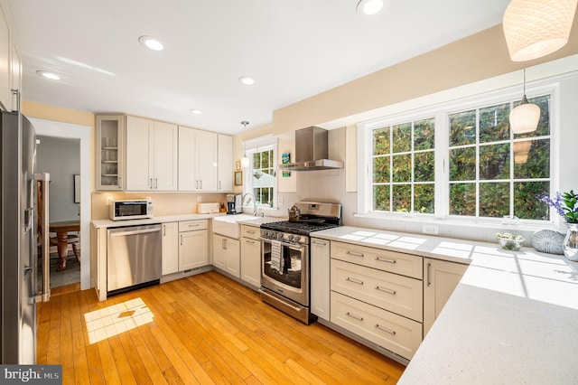 kitchen with light wood finished floors, a sink, appliances with stainless steel finishes, pendant lighting, and exhaust hood