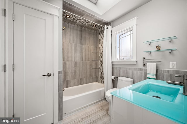 bathroom with tile walls, toilet, wainscoting, shower / bath combination with curtain, and vanity