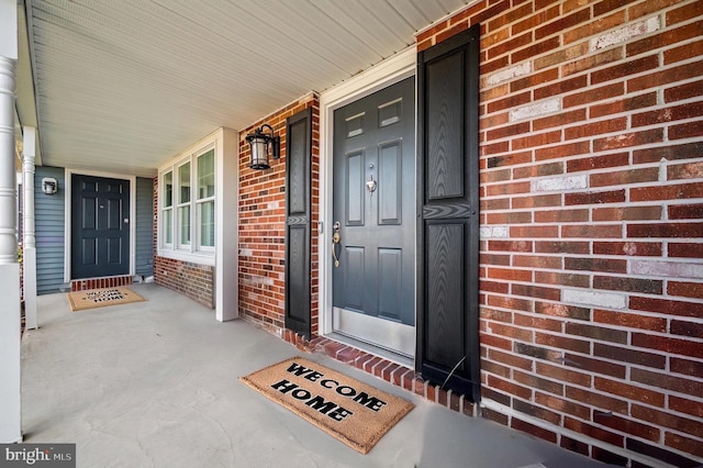 view of exterior entry featuring brick siding and covered porch