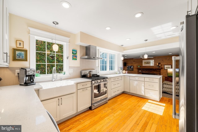 kitchen with wooden walls, appliances with stainless steel finishes, plenty of natural light, wall chimney exhaust hood, and a sink