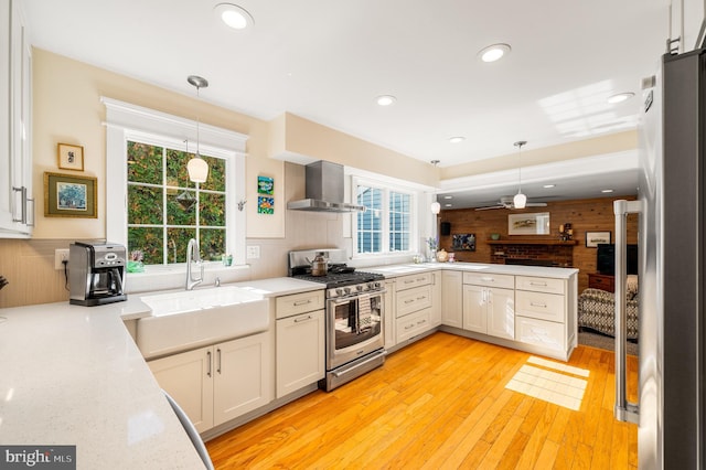 kitchen featuring wooden walls, light wood-style flooring, stainless steel appliances, wall chimney exhaust hood, and a sink