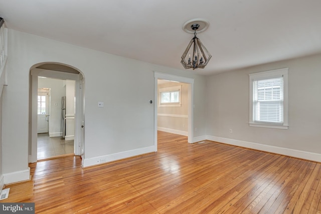 empty room featuring plenty of natural light, light wood-type flooring, and an inviting chandelier