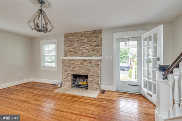 unfurnished living room with hardwood / wood-style flooring, a stone fireplace, and a chandelier