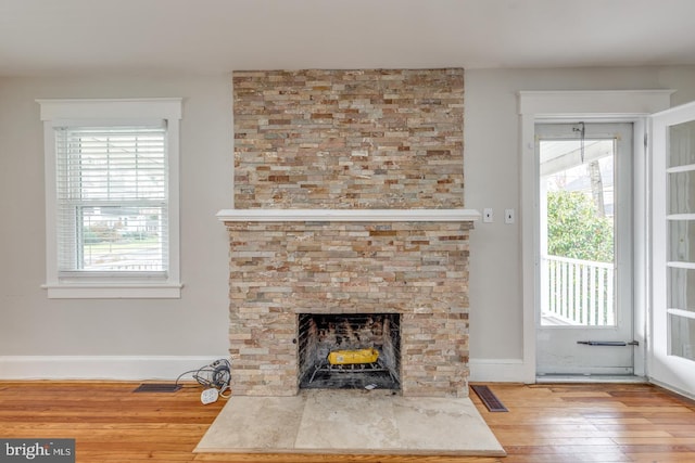 unfurnished living room featuring hardwood / wood-style flooring, a healthy amount of sunlight, and a stone fireplace