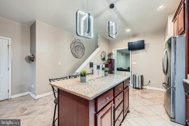 kitchen featuring light stone countertops, stainless steel fridge, pendant lighting, a center island, and a breakfast bar area