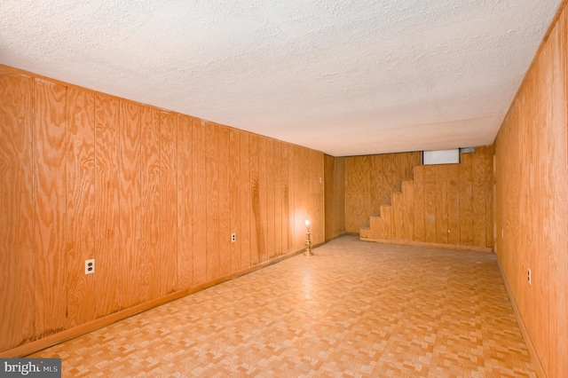 spare room with a textured ceiling, light parquet flooring, and wood walls