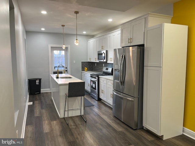 kitchen with white cabinetry, sink, stainless steel appliances, pendant lighting, and a center island with sink