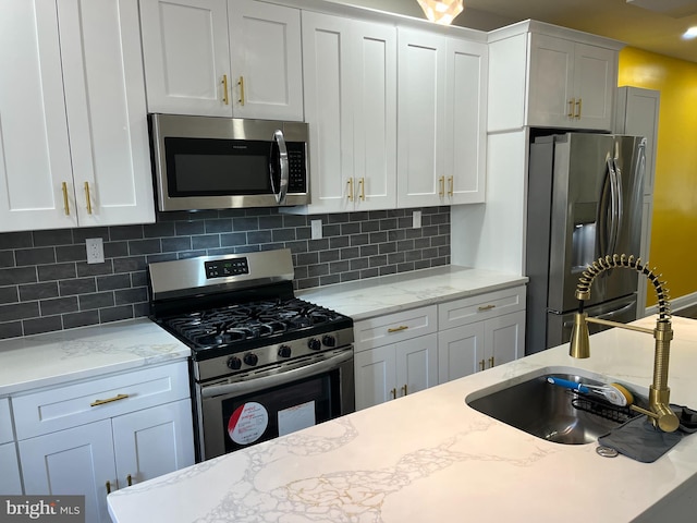 kitchen with backsplash, white cabinets, sink, light stone counters, and stainless steel appliances