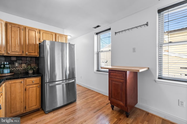 kitchen with stainless steel refrigerator, decorative backsplash, and light hardwood / wood-style flooring