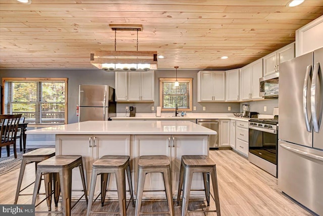 kitchen with appliances with stainless steel finishes, decorative light fixtures, a kitchen island, and a wealth of natural light