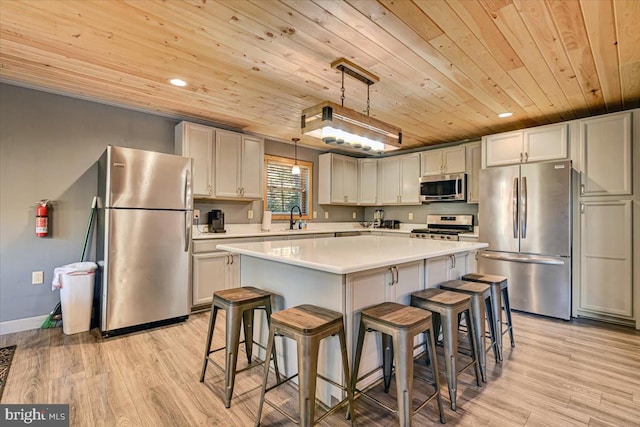 kitchen with appliances with stainless steel finishes, light hardwood / wood-style floors, a kitchen island, and hanging light fixtures