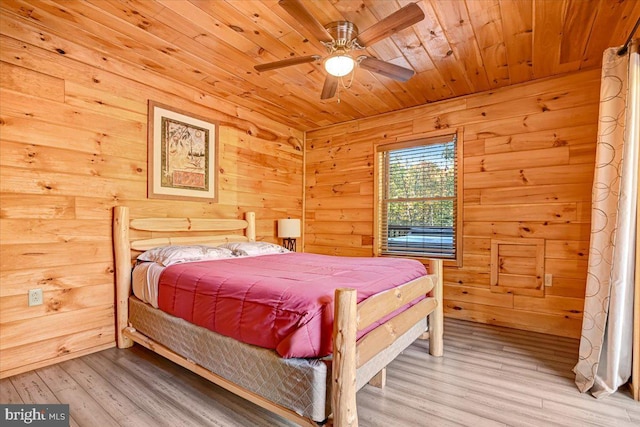 bedroom featuring ceiling fan, light hardwood / wood-style floors, wood ceiling, and wooden walls