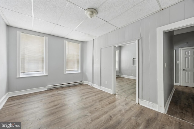 unfurnished room featuring hardwood / wood-style floors, a paneled ceiling, and baseboard heating