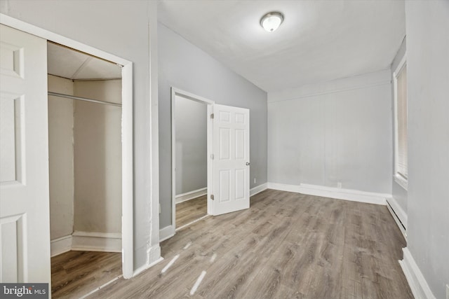 unfurnished bedroom with a closet, a baseboard radiator, and light wood-type flooring