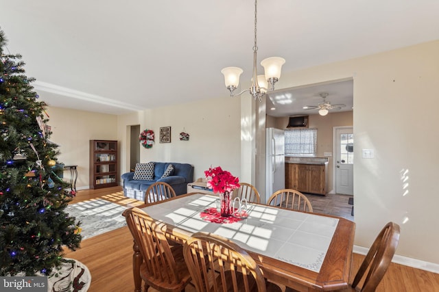 dining space with ceiling fan with notable chandelier and light hardwood / wood-style flooring