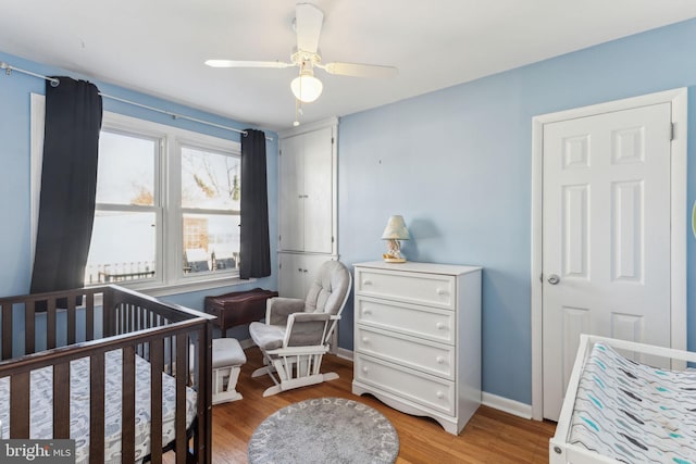 bedroom with ceiling fan, wood-type flooring, and a nursery area