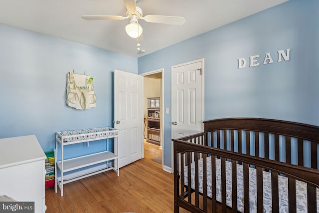 bedroom featuring ceiling fan, hardwood / wood-style floors, and a nursery area