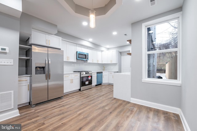 kitchen featuring light wood-type flooring, white cabinetry, hanging light fixtures, and appliances with stainless steel finishes