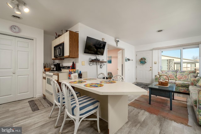 kitchen featuring a breakfast bar area, kitchen peninsula, light hardwood / wood-style flooring, and white range