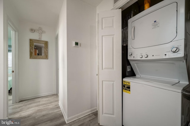 laundry room featuring stacked washing maching and dryer and light hardwood / wood-style floors