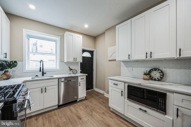 kitchen with light stone countertops, white cabinetry, sink, light hardwood / wood-style flooring, and appliances with stainless steel finishes