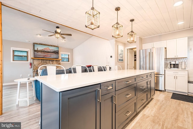 kitchen featuring pendant lighting, a center island, a kitchen bar, white cabinetry, and stainless steel refrigerator