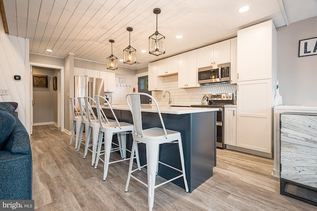 kitchen with hanging light fixtures, stainless steel appliances, light hardwood / wood-style flooring, a breakfast bar, and white cabinets