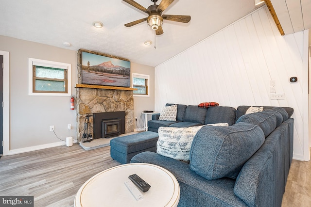 living room with lofted ceiling, ceiling fan, a wood stove, and light hardwood / wood-style flooring