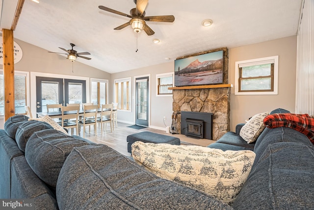 living room with a textured ceiling, ceiling fan, light hardwood / wood-style floors, a wood stove, and lofted ceiling