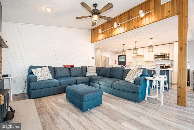 living room featuring light wood-type flooring, ceiling fan, and wooden walls