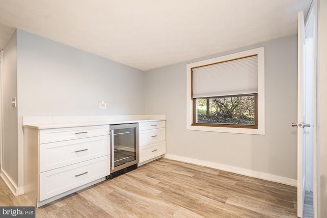 kitchen with light wood-type flooring, white cabinetry, and beverage cooler